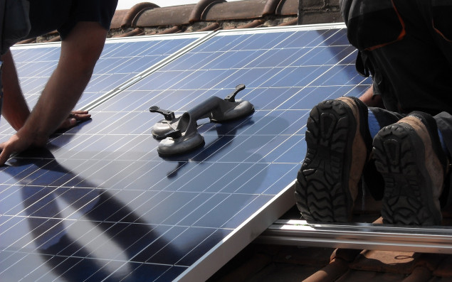 Photovoltaik-Anlage auf einem Dach und darauf arbeitende Techniker.